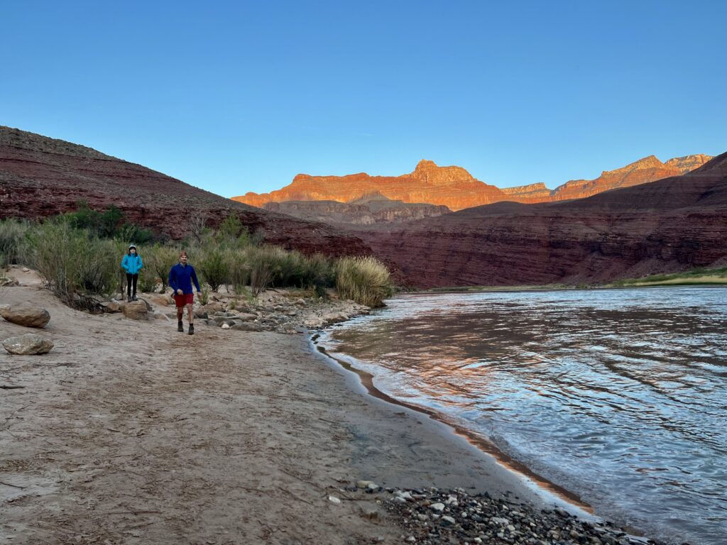 Hikers walk on a beach by the Colorado River.