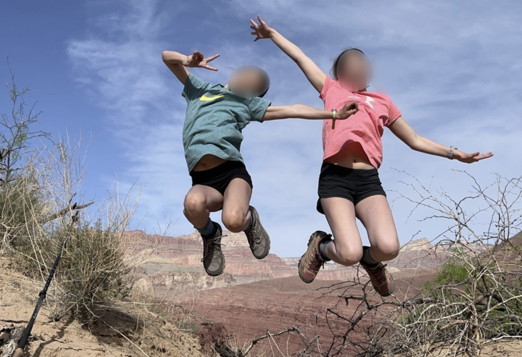 People jump on a bluff with a canyon wall backdrop.