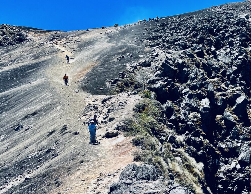 Hikers descend a steep volcanic slope in a line.