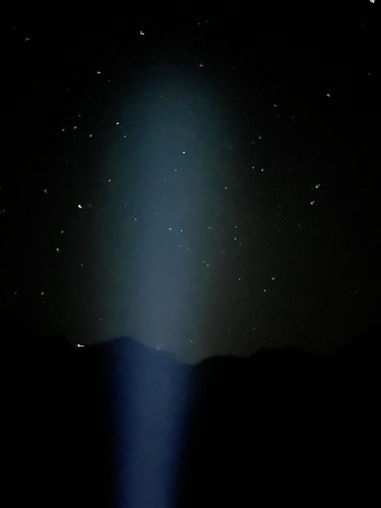 A headlamp's beam illuminates a starry sky.