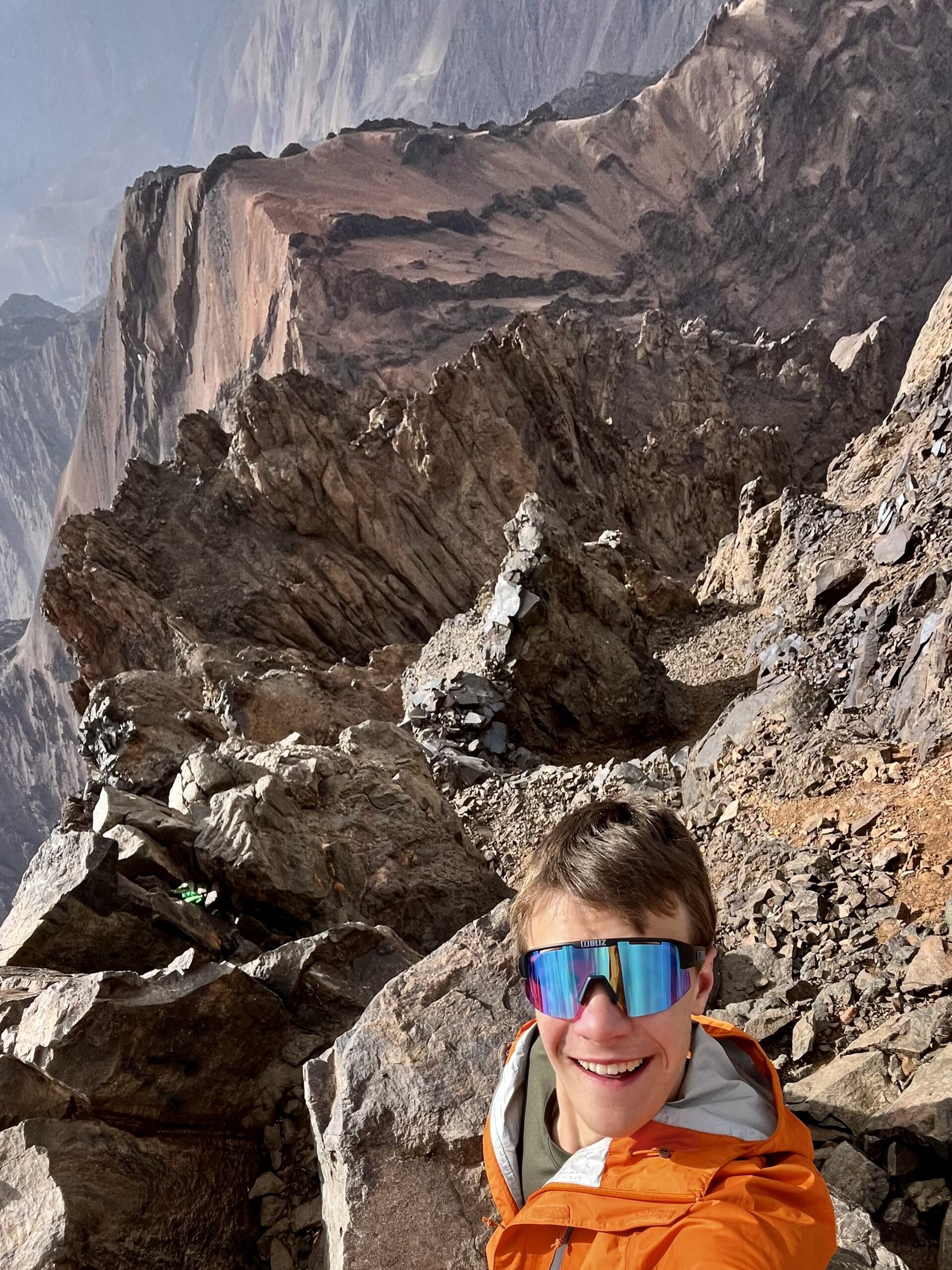 A guy takes a selfie while lying on a rock outcropping over a cliff.